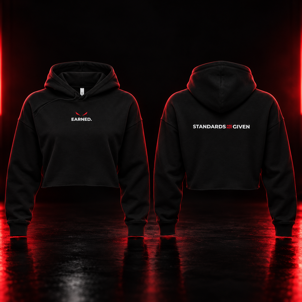 Black cropped hoodies shown from the front and back on a dark reflective studio floor with red lighting. The front hoodie has a small white 'EARNED.